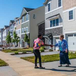 Two people shaking hands in a driveway with condos in the background