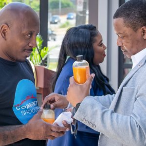 Man in a suit hands another man a bottle of pressed juice