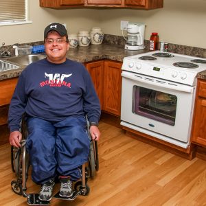 Man in a wheelchair smiles for the camera in a kitchen with low counters