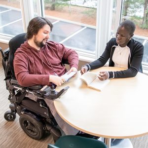 A man in a wheelchair works at a table with a woman