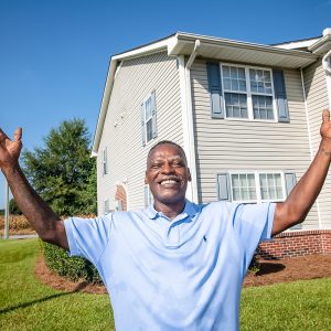 Man stands in front of housing units smiling with his hands in the air