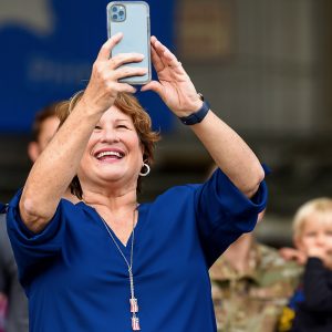 Woman smiles and holds up her cell phone to take a photo of something out of frame