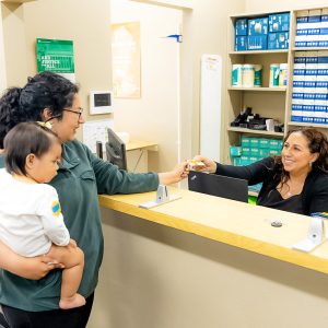 Woman holding a child hands insurance card to receptionist in a health clinic