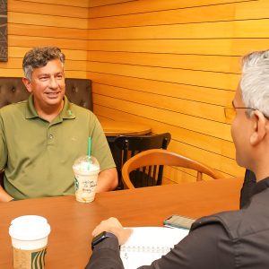 Two men sit across the table from each other with Starbucks coffees