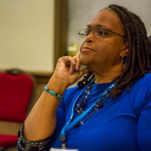 Woman sits with her hand against her cheek in a thinking pose