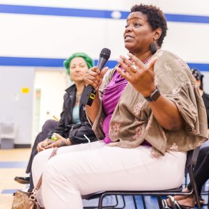 Woman speaking into a microphone in a gym auditorium