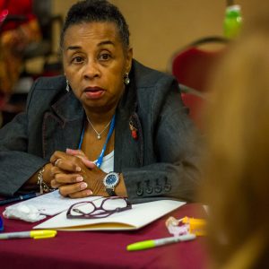 Woman sitting at event table with her hands crossed listening to someone else speak