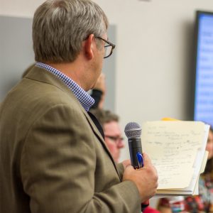 Man holding a folder and speaking into a microphone